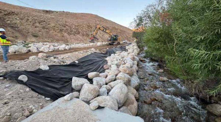 View of shoulder of road lined with tarps and boulders while a man in neon construction gear looks on.